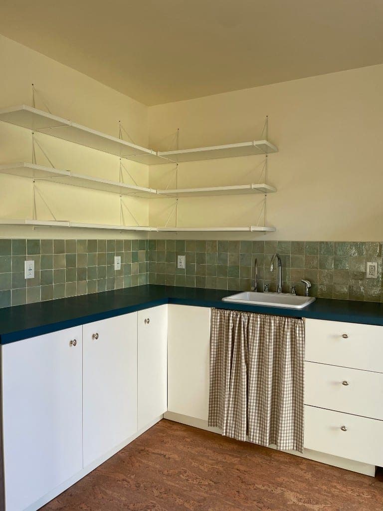 West Side Santa Barbara ADU kitchen with teal counters, sage tile, chrome faucet, and gingham skirt under the sink