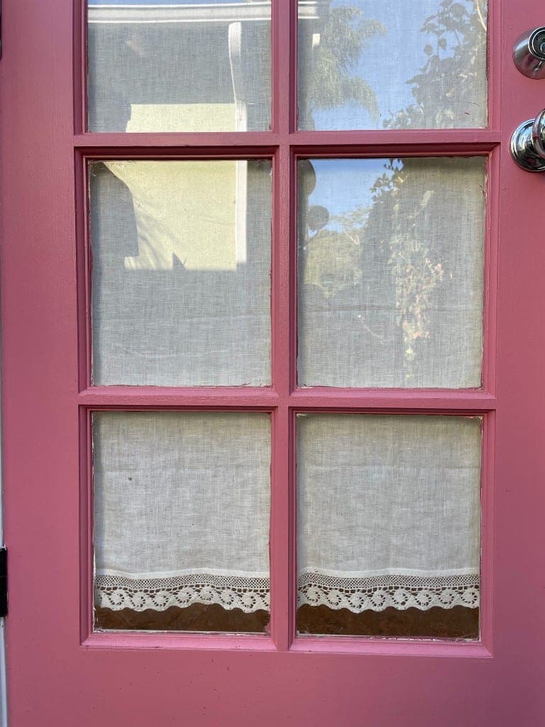 Dusty-pink multi-pane door with lace cafe curtains reflecting Santa Barbara sky and palms