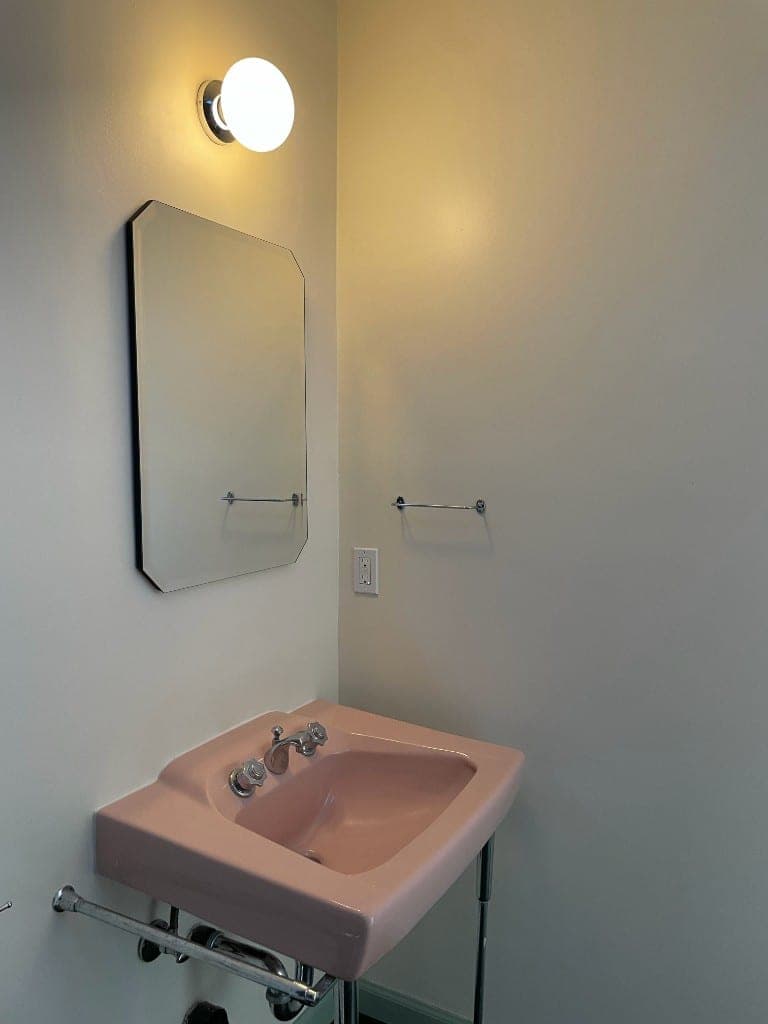 Dusty-pink porcelain console sink with polished chrome legs, cross-handle faucet, and octagonal mirror