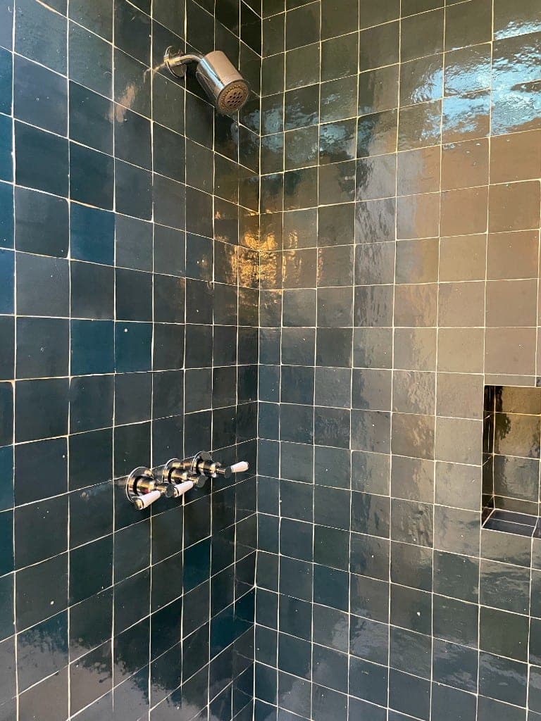 Deep teal zellige shower with chrome showerhead, white ceramic lever handles, and a tiled niche