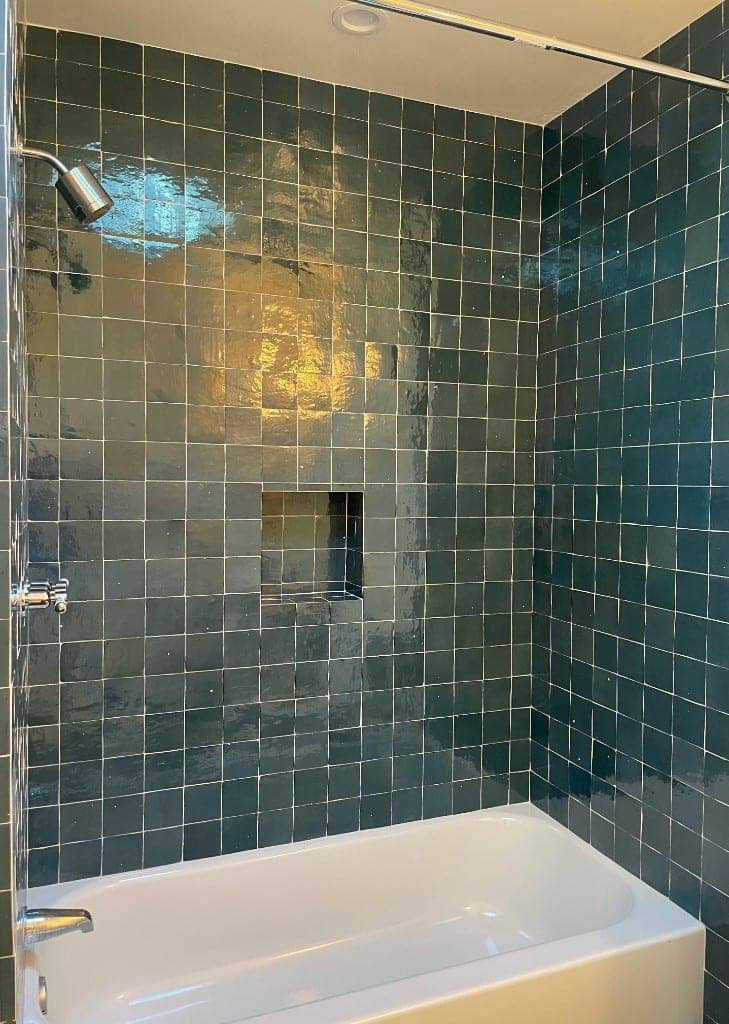 White bathtub-shower with glossy teal tile, chrome fixtures, and a recessed niche